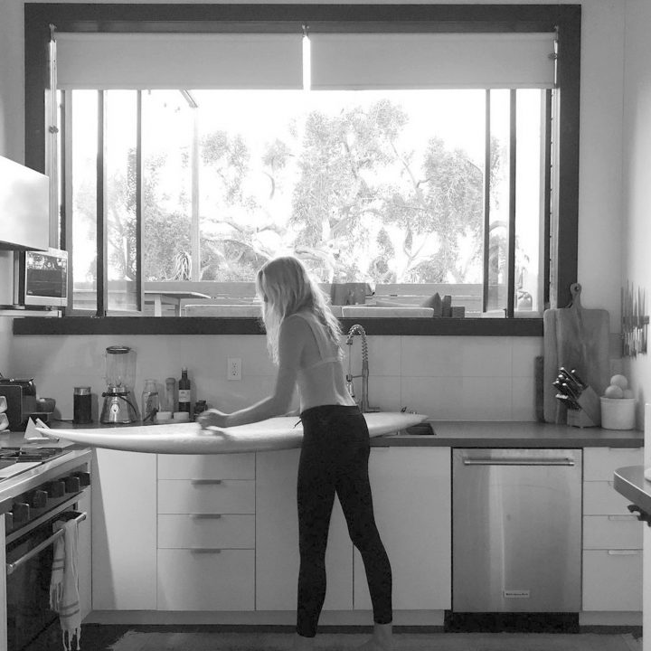 Renee Labbe cleaning surfboard in her kitchen in black and white