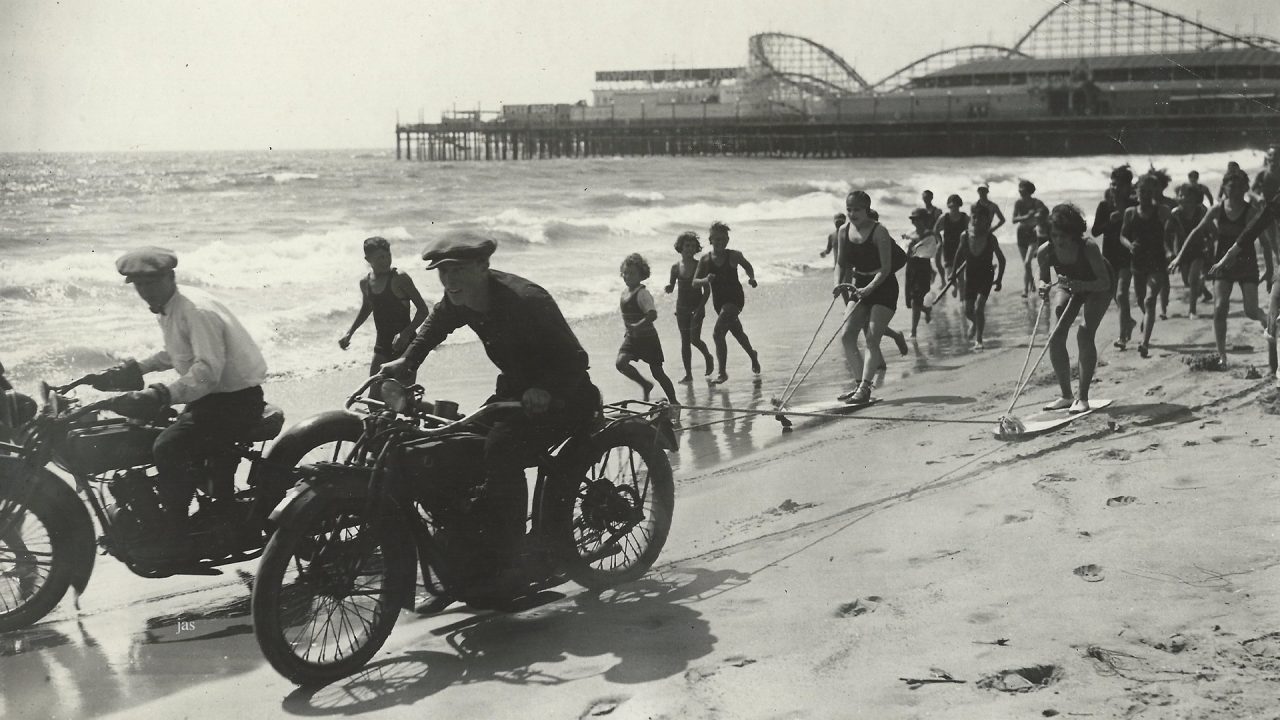 Black and White image of motorcyclists driving down the beach past santa monica pier